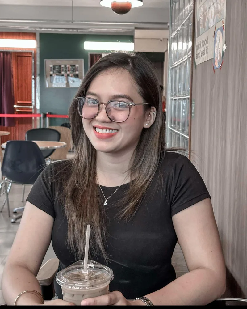 Doreen smiling at a café table, wearing glasses, with an iced coffee in front of her